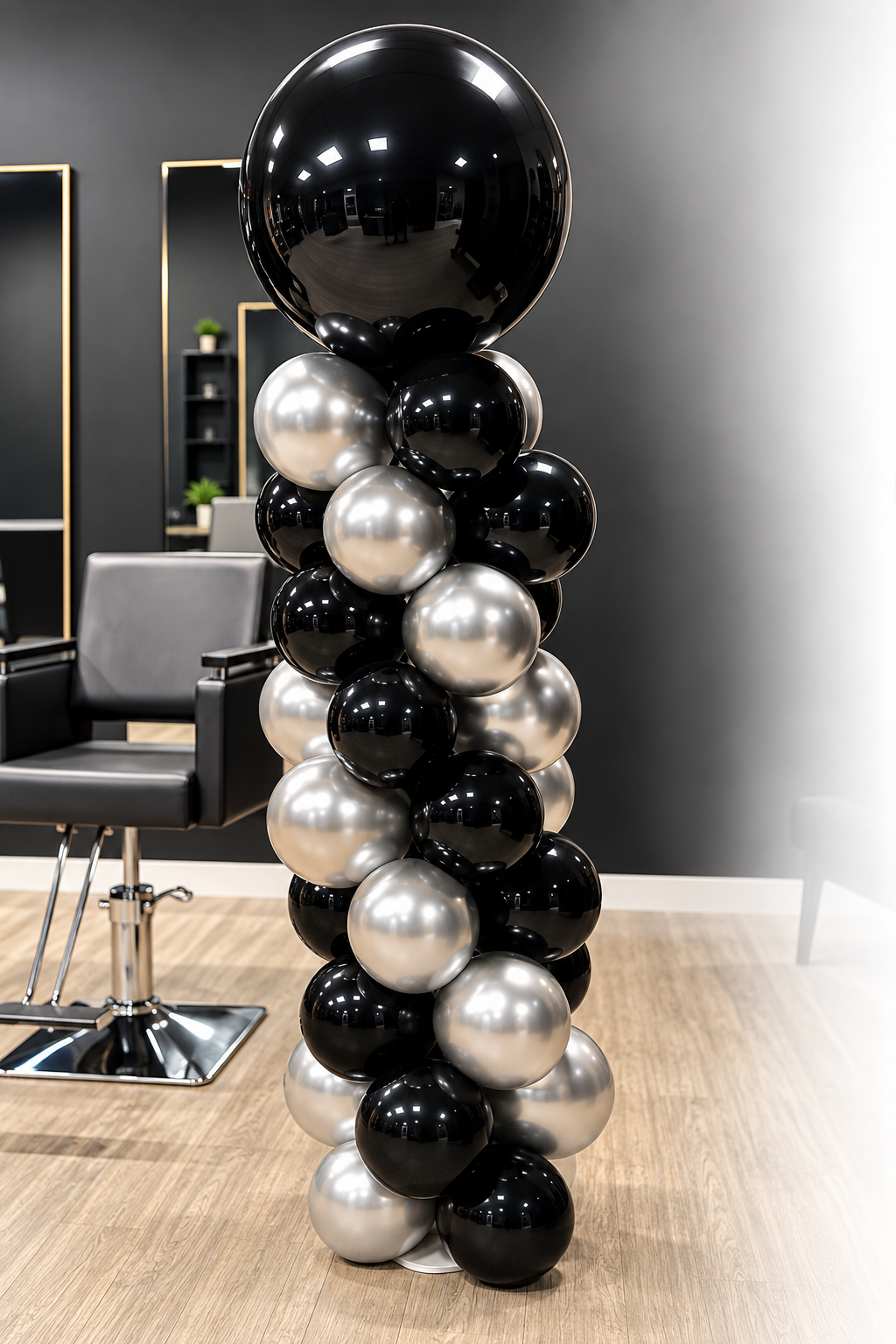 Black, silver, and white balloons arranged in a column, topped with a large black balloon, inside a modern salon.