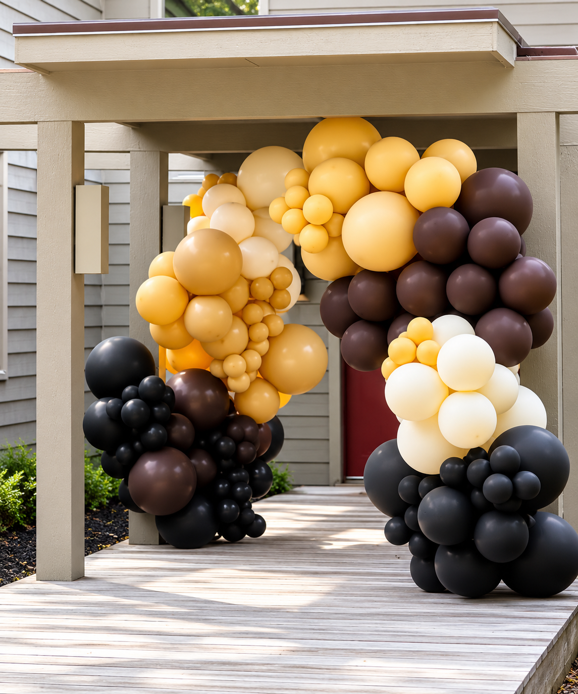 Balloon arch with black, dark brown, cream, and yellow balloons at an outdoor event entrance.