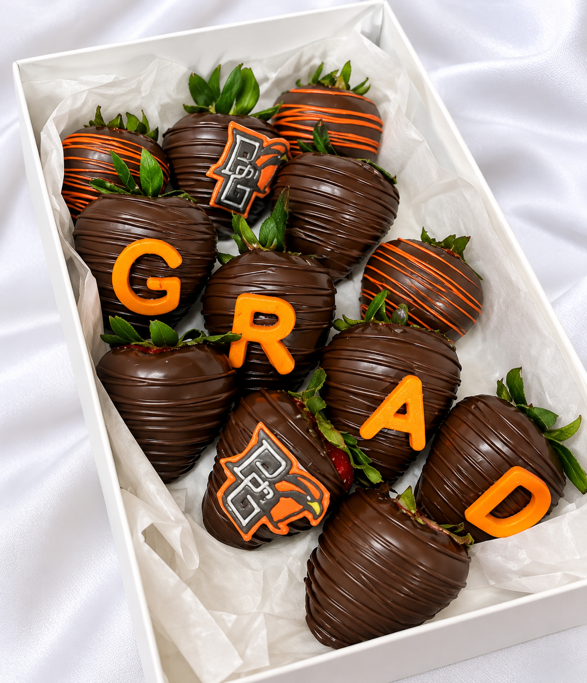 Box of chocolate-covered strawberries with orange and black decorations spelling out 'G' 'R' 'A' 'D'.'}