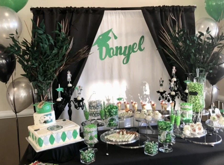 Green, black, and white decorations for a birthday party with a cake, cupcakes, and various treats. The backdrop has the name 'Tanyel'. The table is decorated with green, white, and black themed candies, balloons, and greenery.