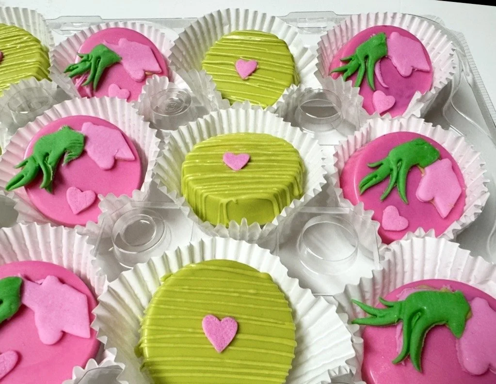 Assorted pink and green chocolate covered oreos with some featuring green dragon or dinosaur shapes and pink hearts.