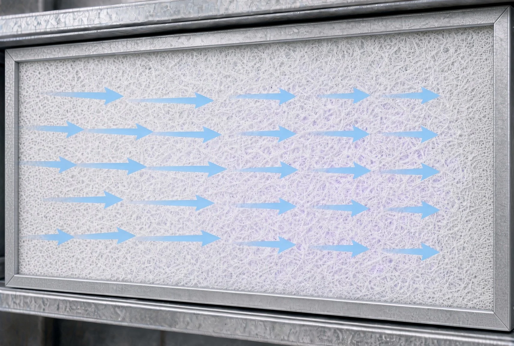 Close-up of TrueSeal air filter system with a white textured filter media and blue arrows indicating airflow direction passing through the filter.