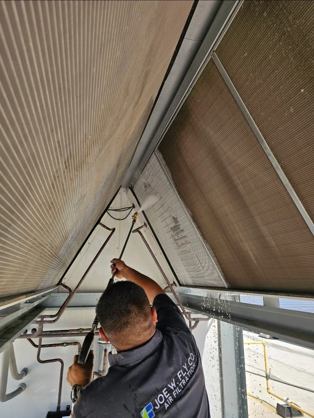 Technician cleaning a large air conditioning or cooling coil with a spray tool inside an industrial facility.