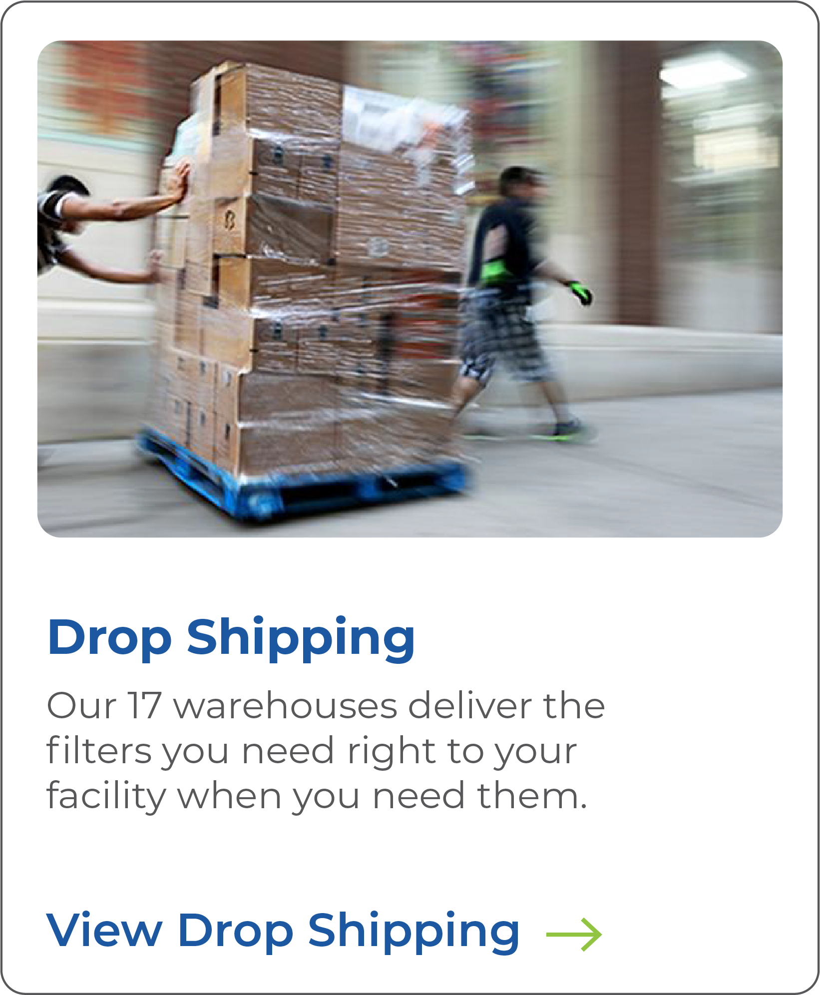 A delivery person pushing a cart loaded with large cardboard boxes wrapped in plastic, moving through a facility with a blurred background.