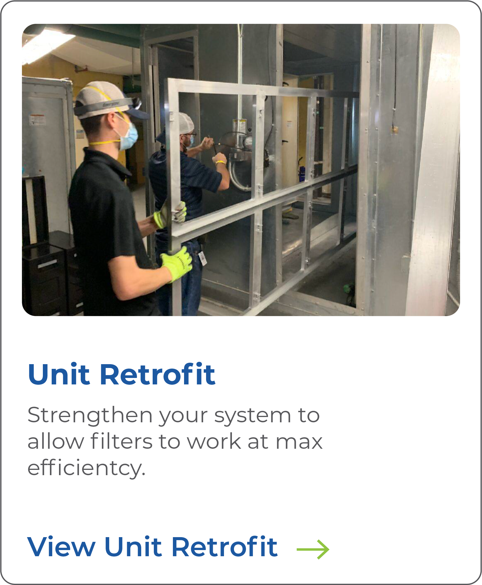 Two workers in construction gear, including face masks and gloves, are retrofitting a j-frame wall within a metal framing structure in a commercial or industrial building.