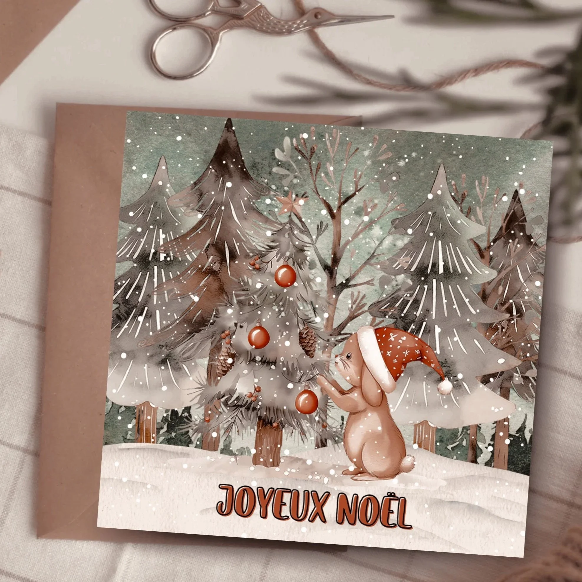 Carte de Noël avec des montagnes enneigées, arbres, un lapin en peluche portant un chapeau, des décorations rouges, et la phrase 'Joyeux Noël' en français.