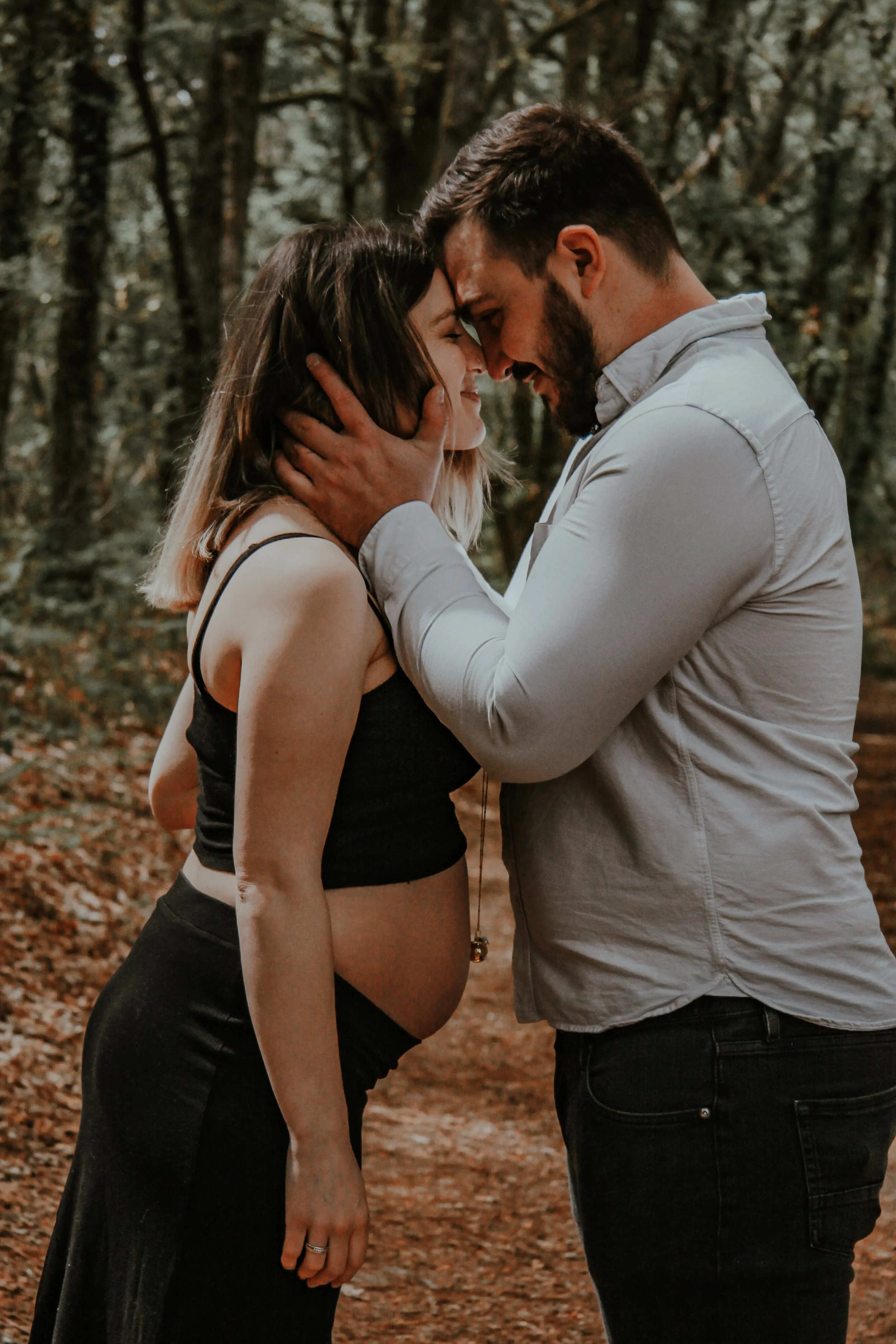 Un homme et une femme face à face dans une forêt, ils se touchent le front et se regardent intensément, partageant un moment intime.