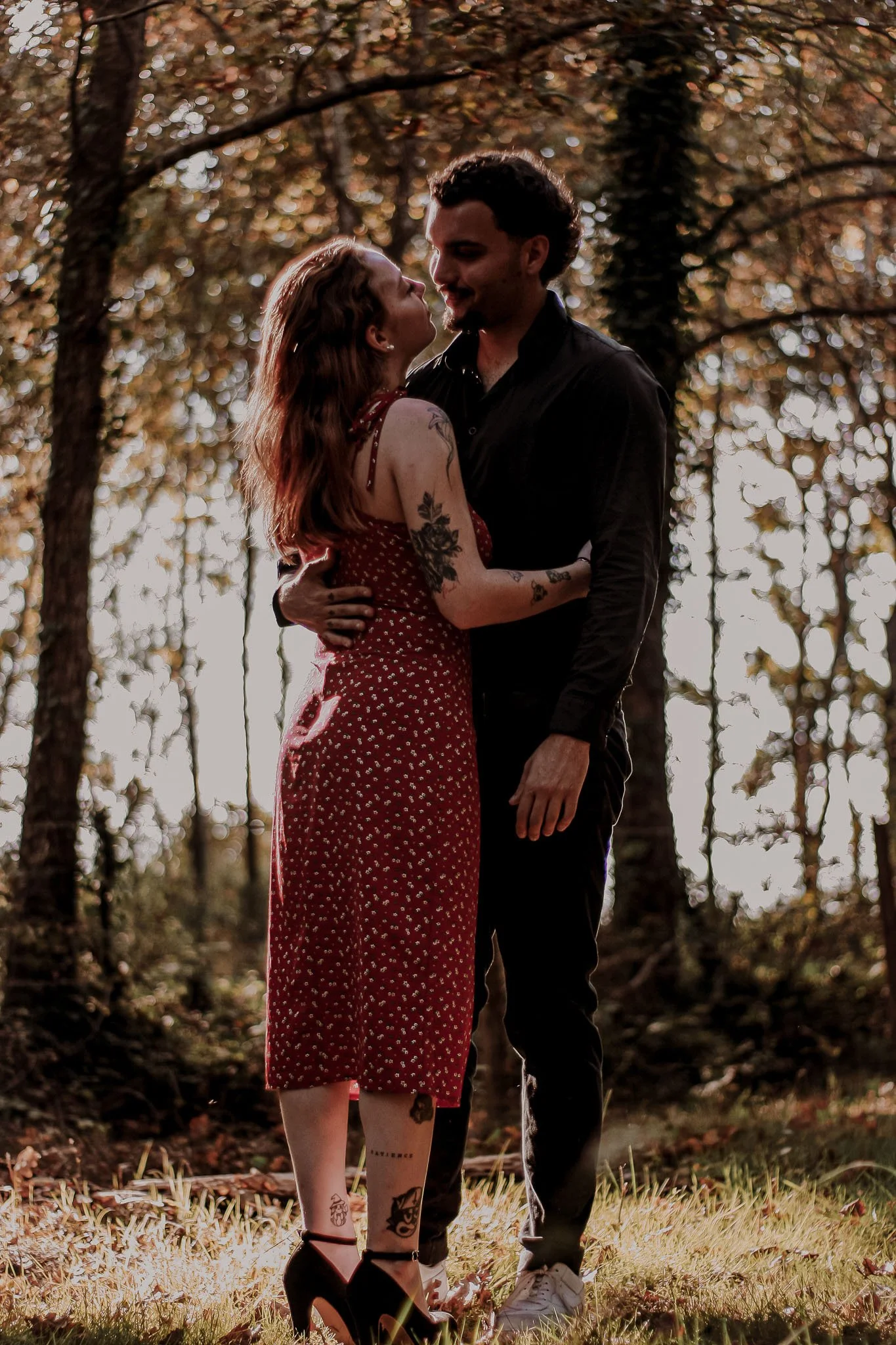 Un couple debout dans une forêt en automne, se regardant tendrement.
