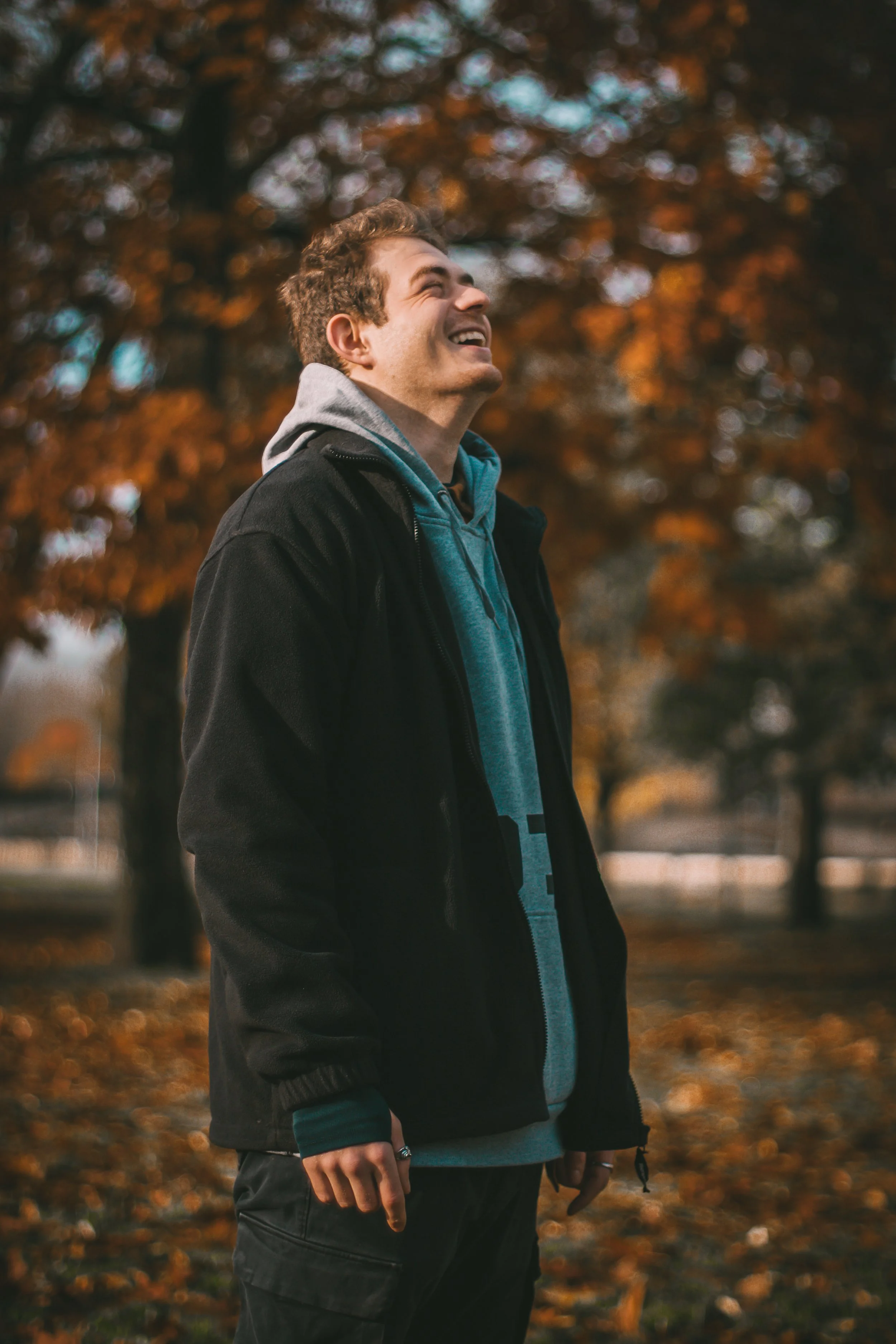 Jeune homme souriant avec des feuilles d'automne en arrière-plan.