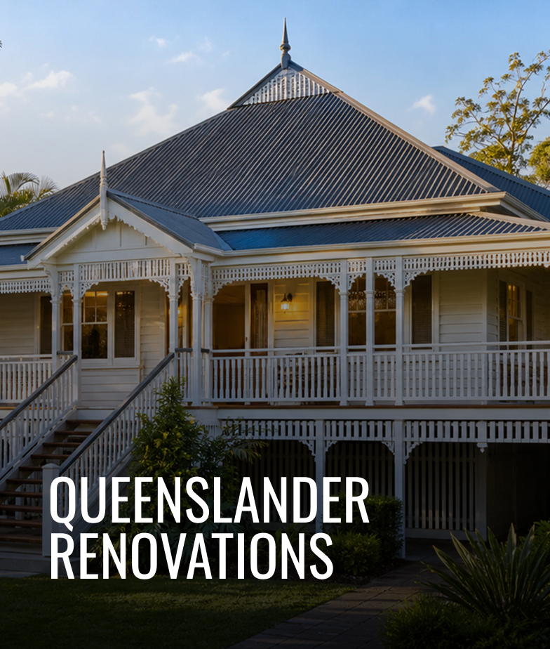 A large Victorian-style house with a white wooden exterior, decorative trim, and a steep metal roof. The house has a wrap-around porch with stairs leading up to it, and outdoor lighting is visible inside. The sky is blue with a few clouds, and lush trees surround the house.