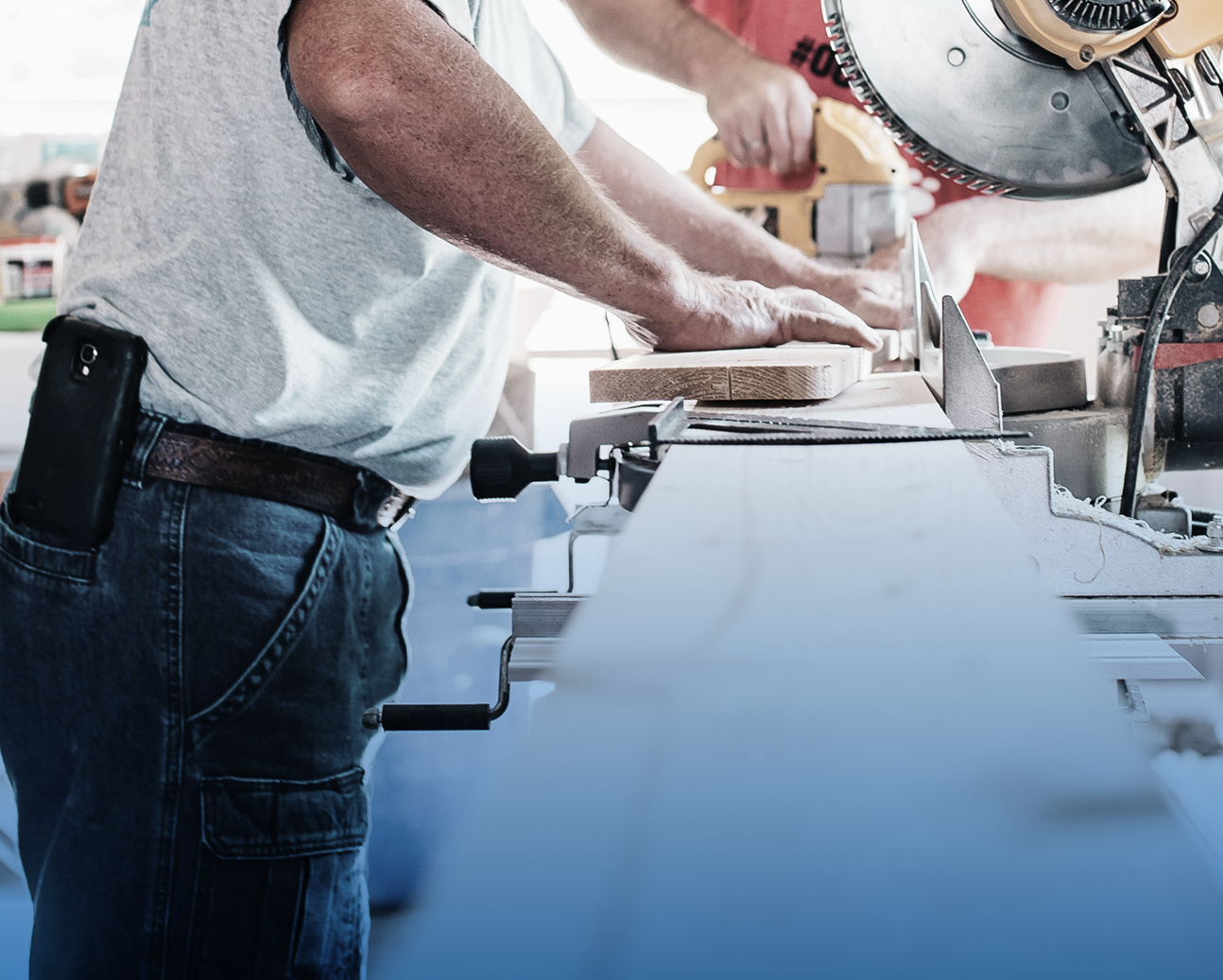 People using a miter saw in a woodworking shop to cut a piece of wood.