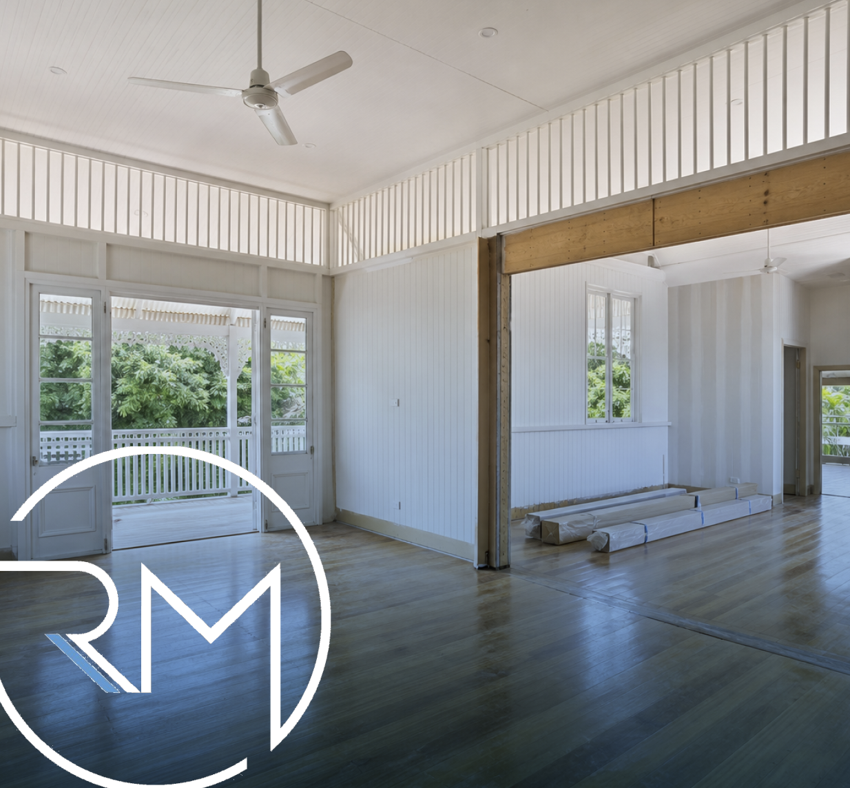 Interior of a house under renovation with white walls, wooden floors, and a large sliding glass door leading to a porch with greenery outside.