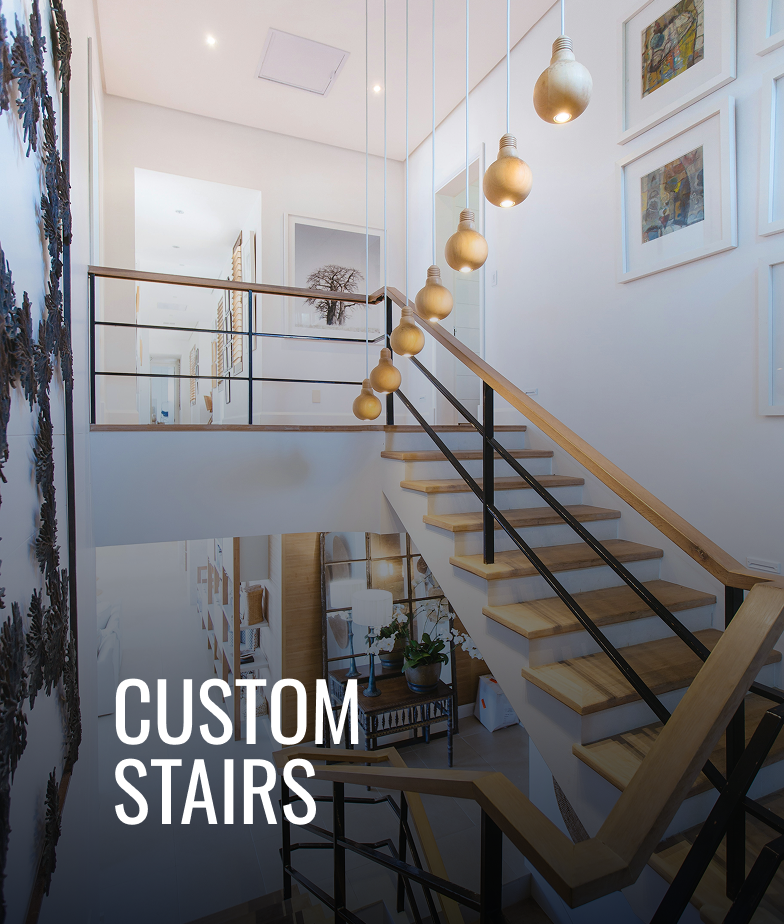 Interior view of a modern staircase with wooden steps, black metal railing, and hanging light fixtures in a bright, decorated home with framed artwork on the walls.
