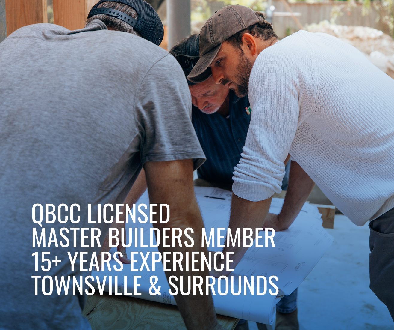 Group of men closely examining architectural plans outdoors, with text overlay about QBCC licensed master builders in Townsville and surrounds.