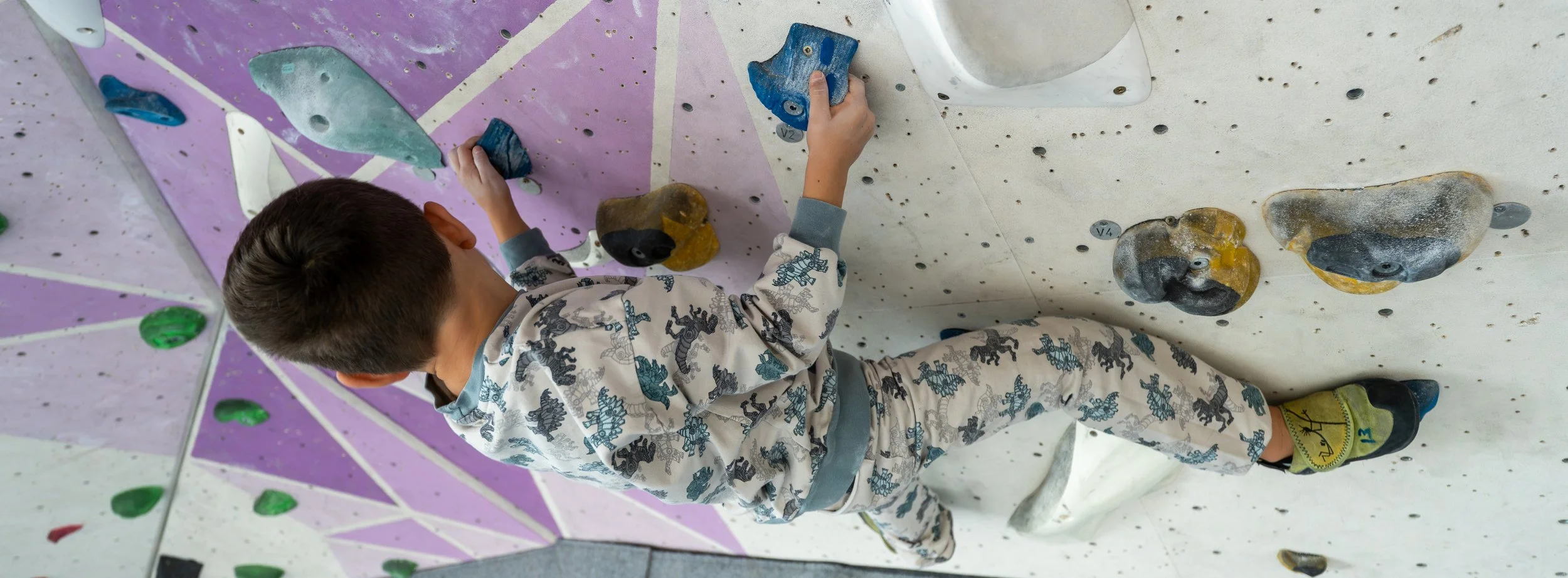 A young child climbing an indoor rock wall with various colored holds.
