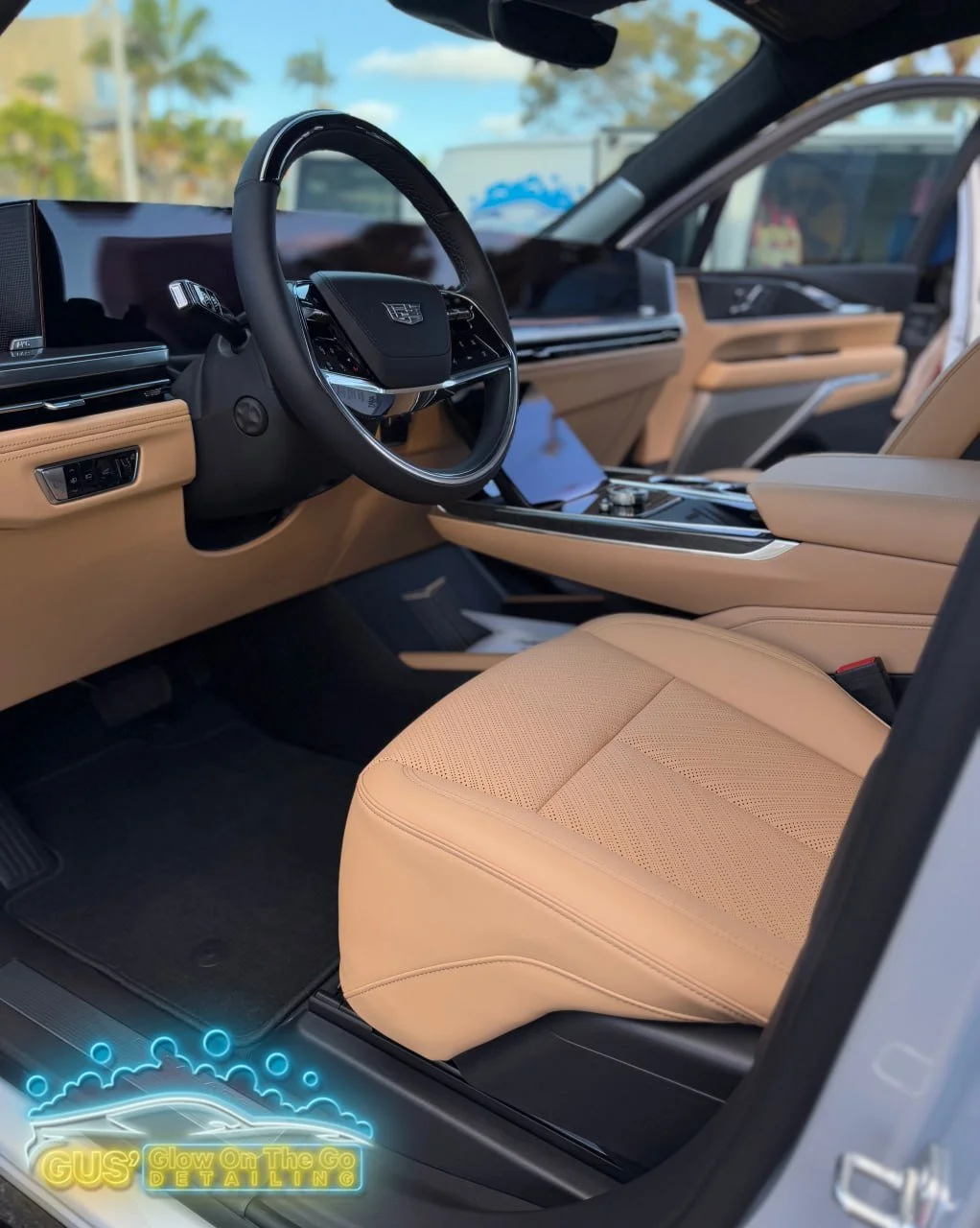 Interior of a luxury car featuring a beige leather seat and a modern dashboard with a steering wheel that has a badge logo, window views of trees and a blue sky outside.