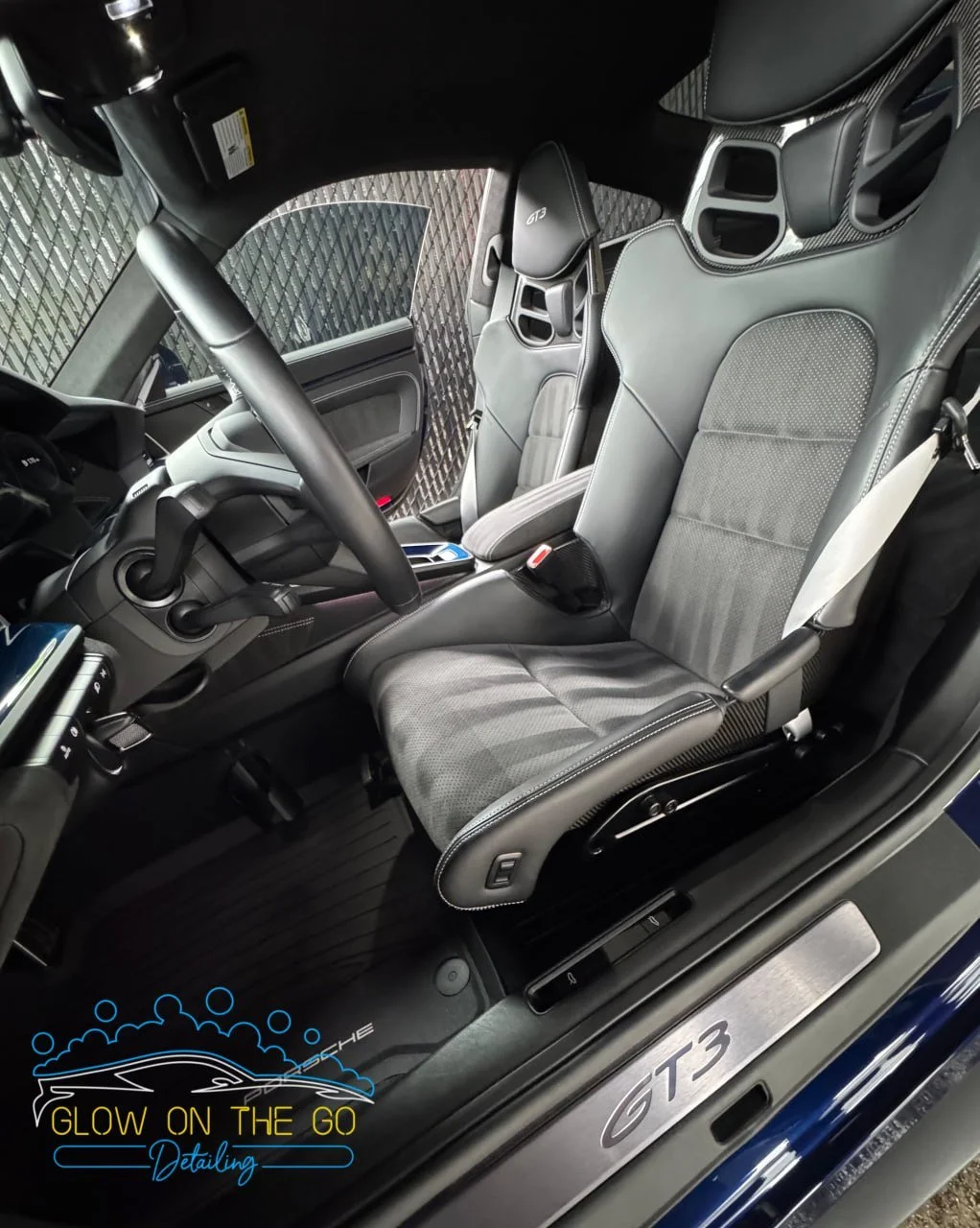 The interior of a Porsche GT3 sports car, featuring a sporty seat with a GT3 logo, a steering wheel, and a view of the dashboard and door panel.