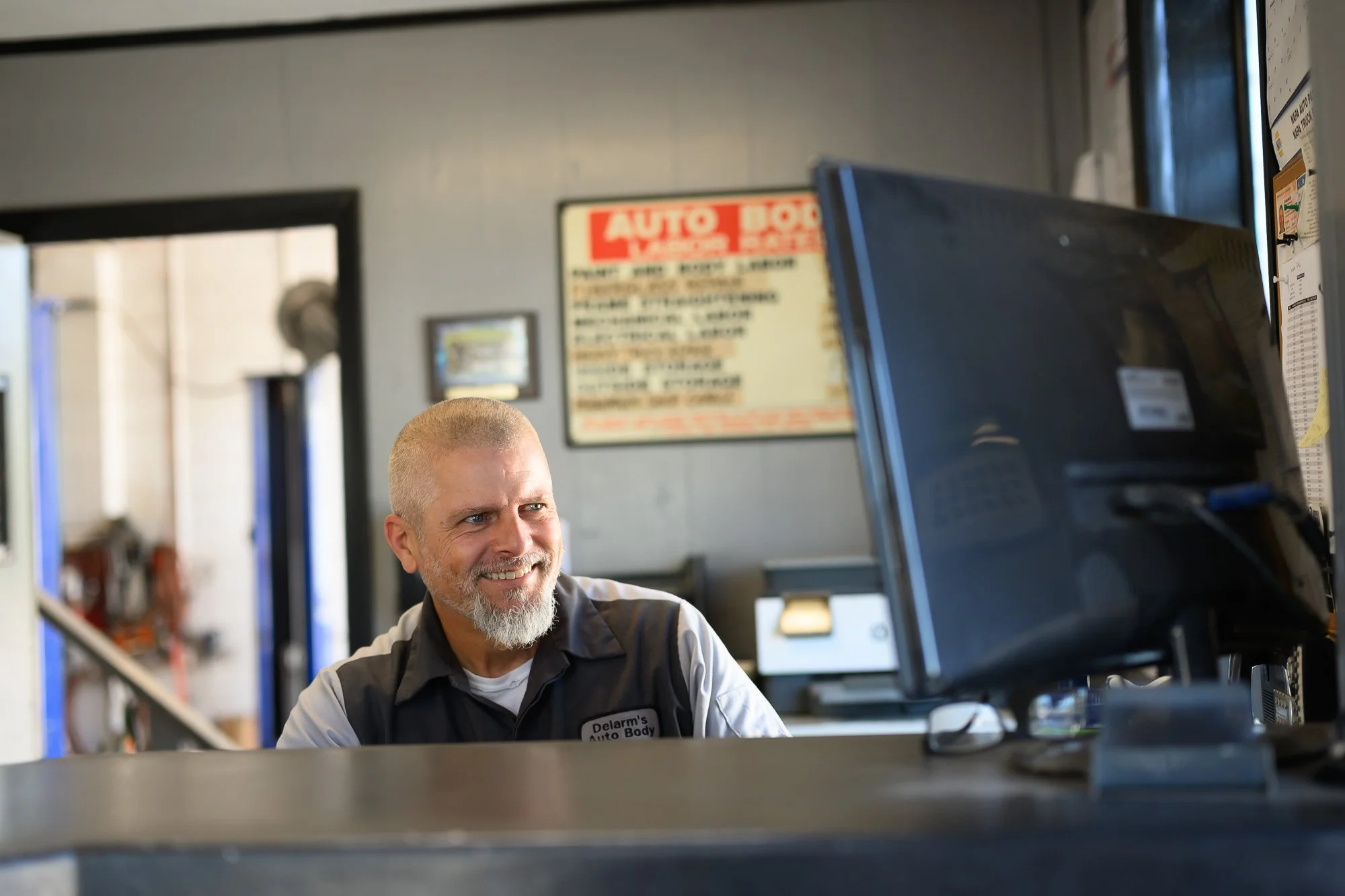 Smiling man with a beard at auto repair shop working on a computer.