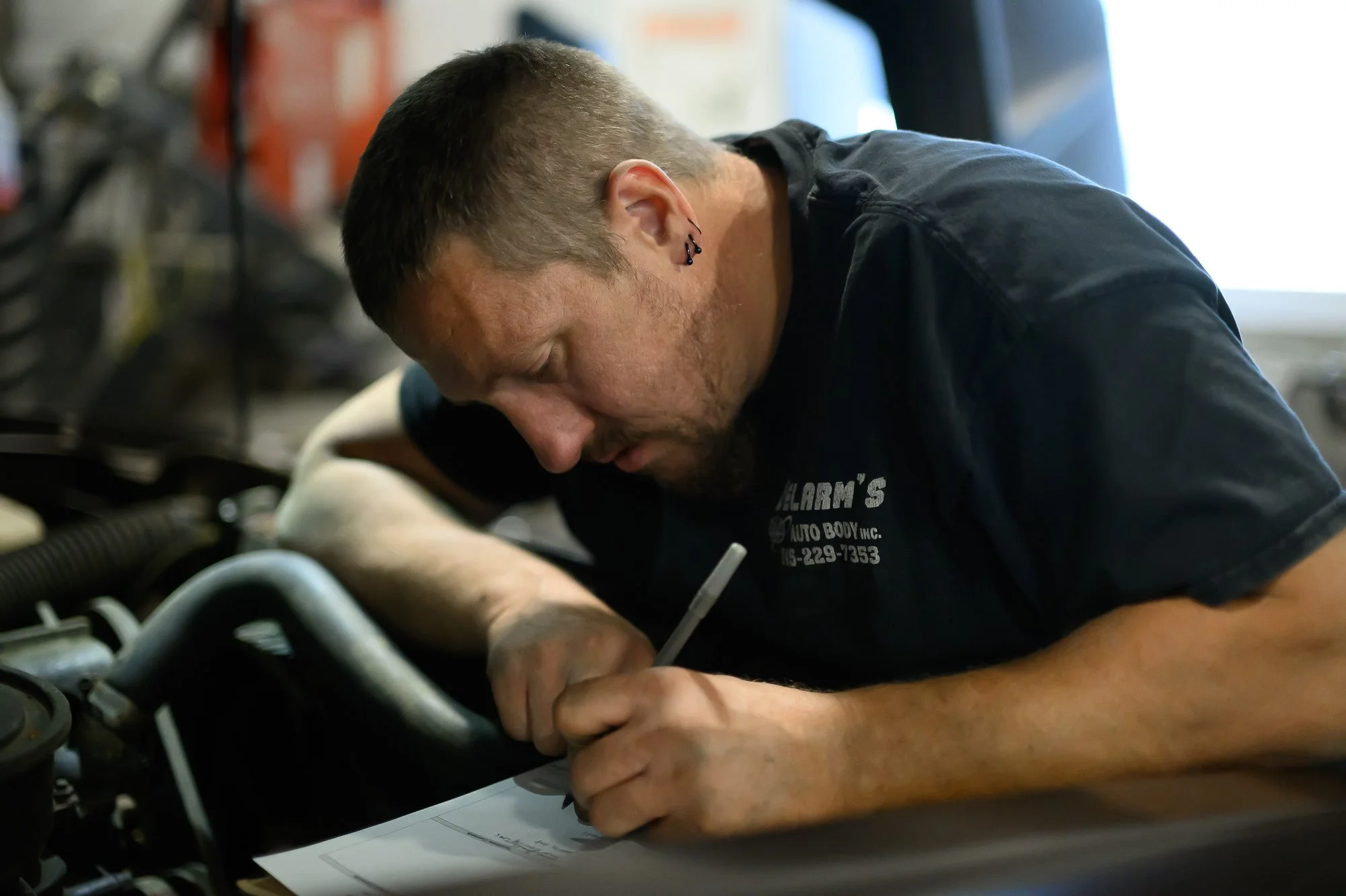 A mechanic is working under the hood of a car, inspecting or repairing the engine in a garage.