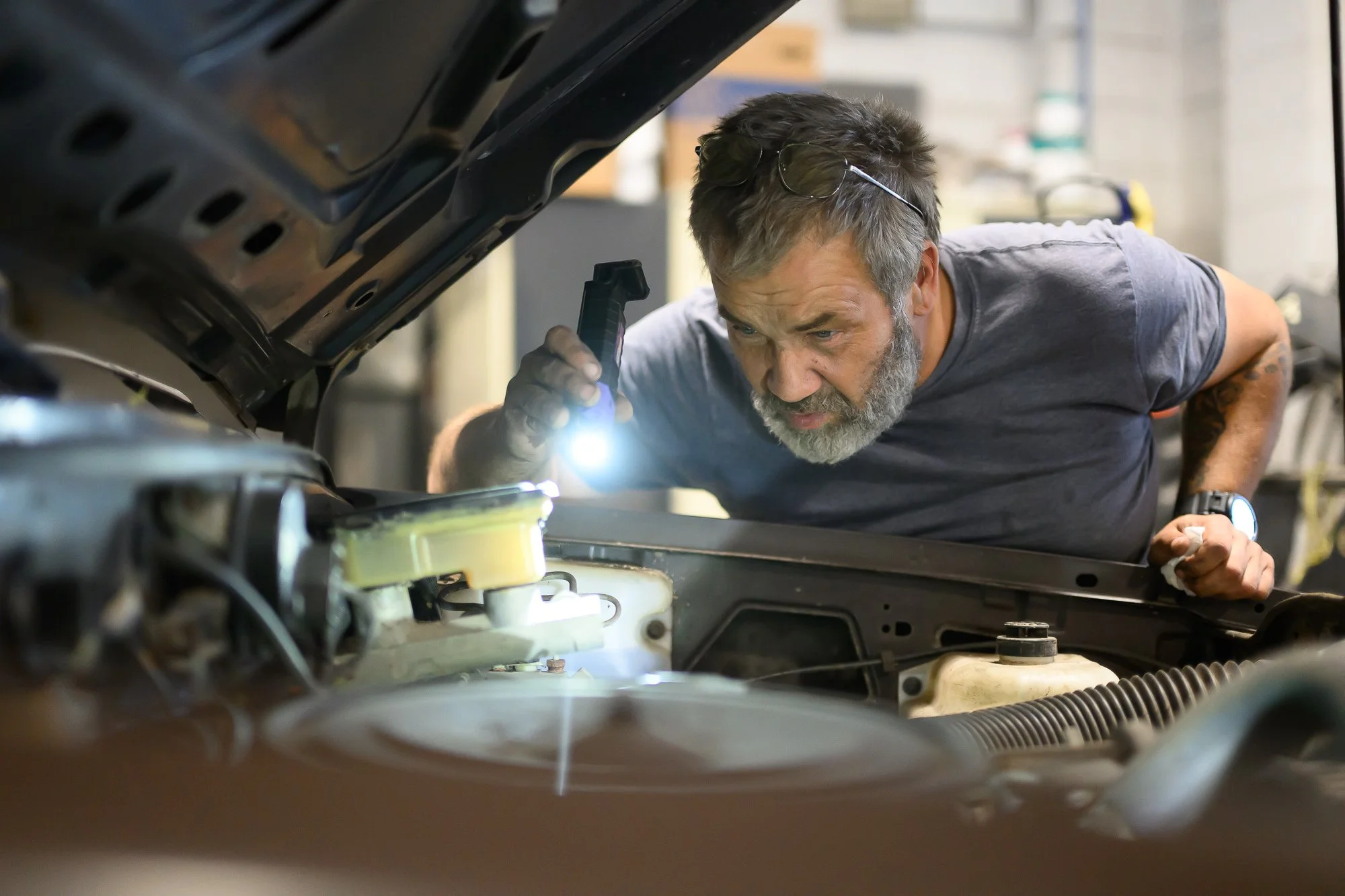 John working under a raised hood with a flashlight