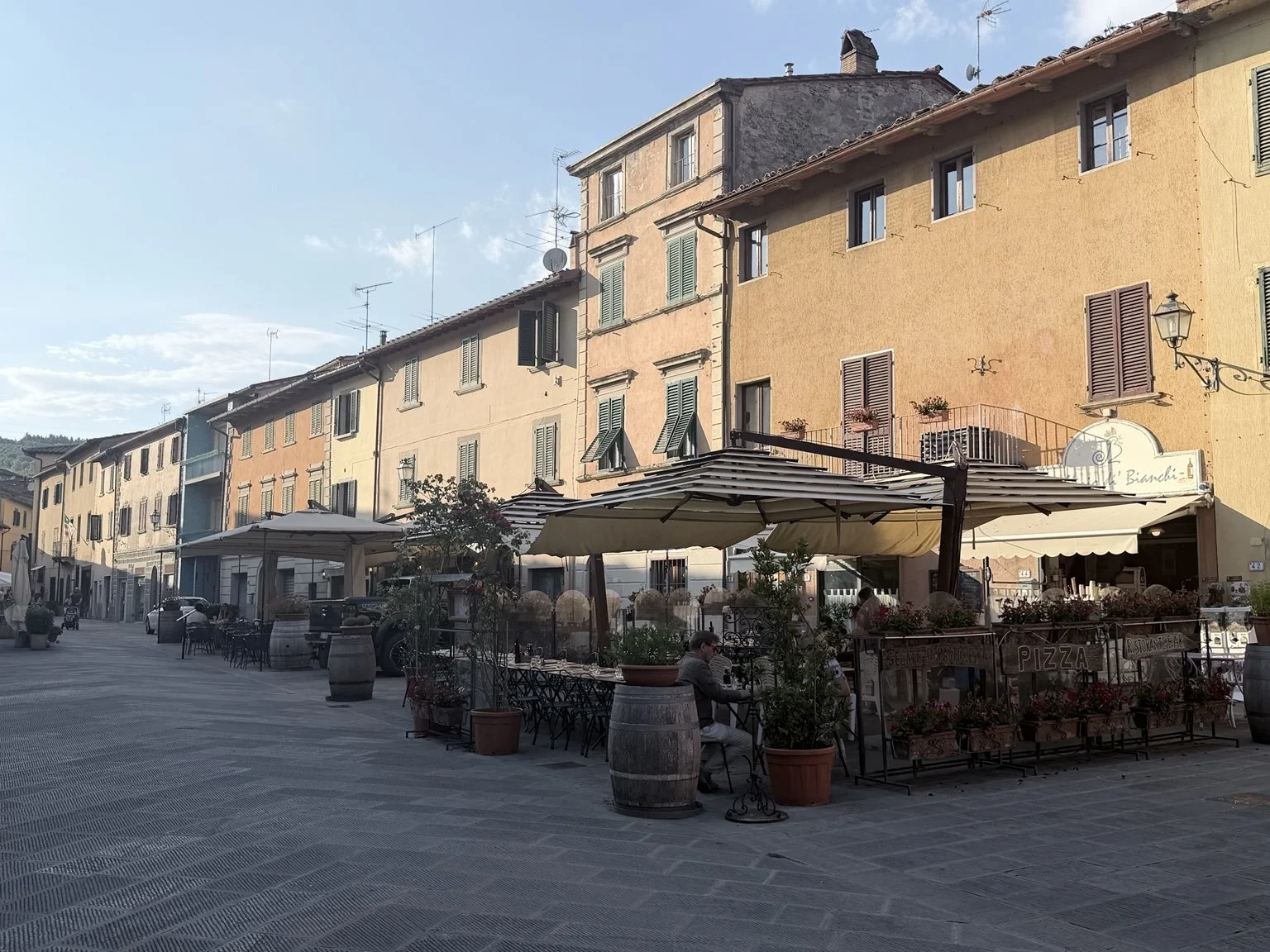 Outdoor restaurants and historic buildings surrounding the village piazza in Gaiole in Chianti, Tuscany, Italy.