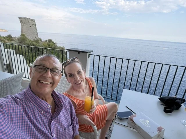 Couple enjoying drinks on a boutique hotel terrace overlooking the Mediterranean Sea in Praiano, Italy.