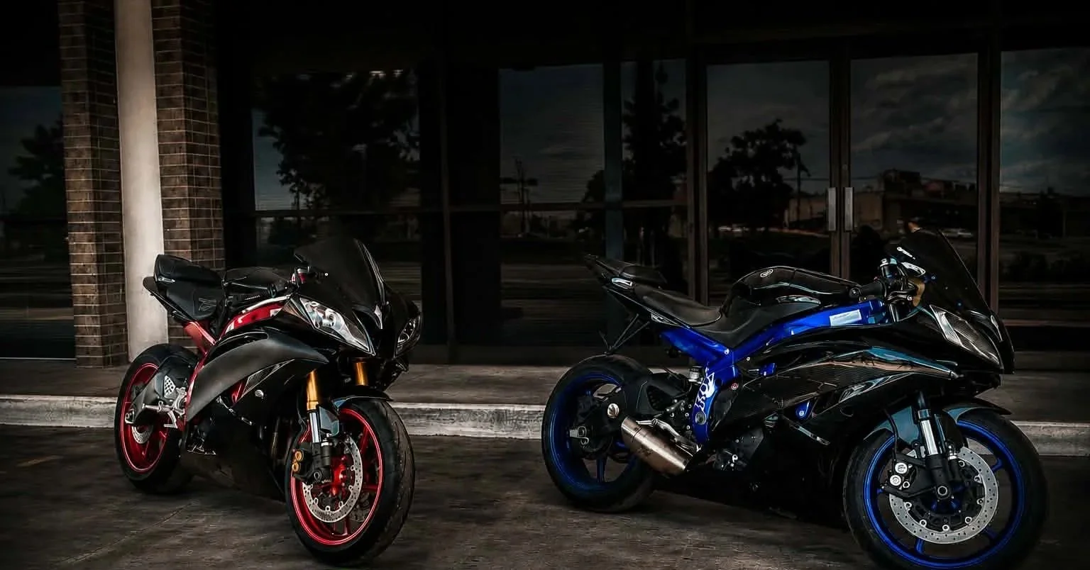 Two sport motorcycles parked outside a building at night, one black and red and the other black and blue.