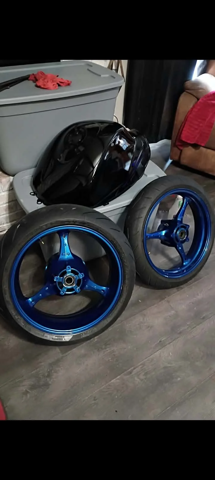 Blue motorcycle wheels with tires leaning against a plastic bin.