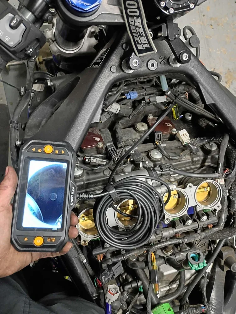 A mechanic's hand holding a diagnostic scan tool over an engine with throttle bodies, wires, sensors, and electrical connectors.