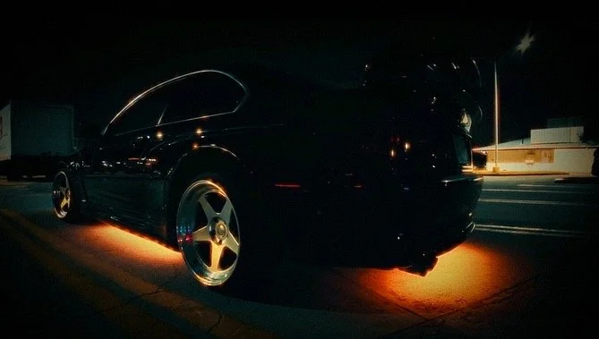 A black sports car with illuminated underglow lights parked at night on a road.