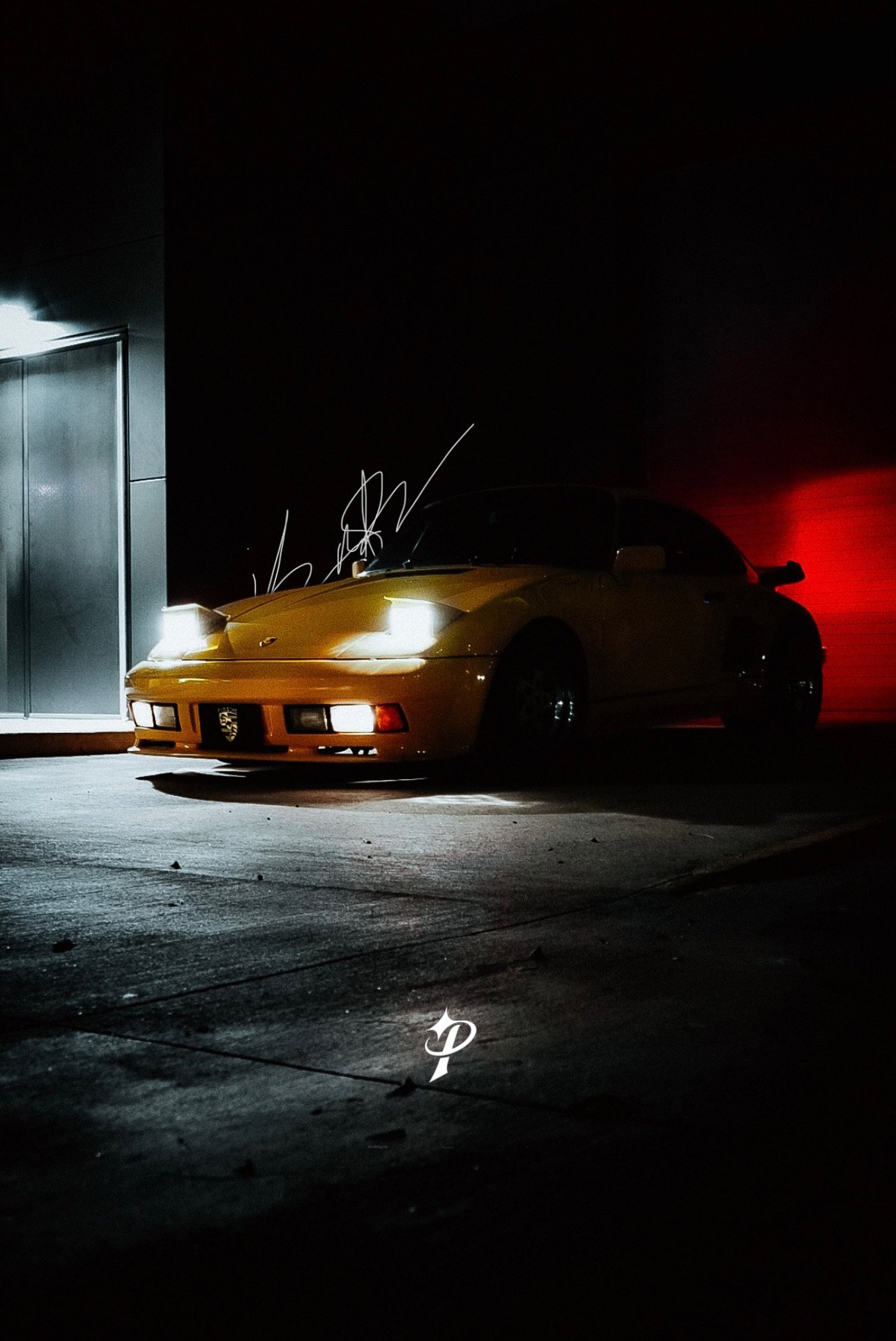 Yellow sports car parked in a dimly lit area at night, with a black background and a faint red light on the right side.