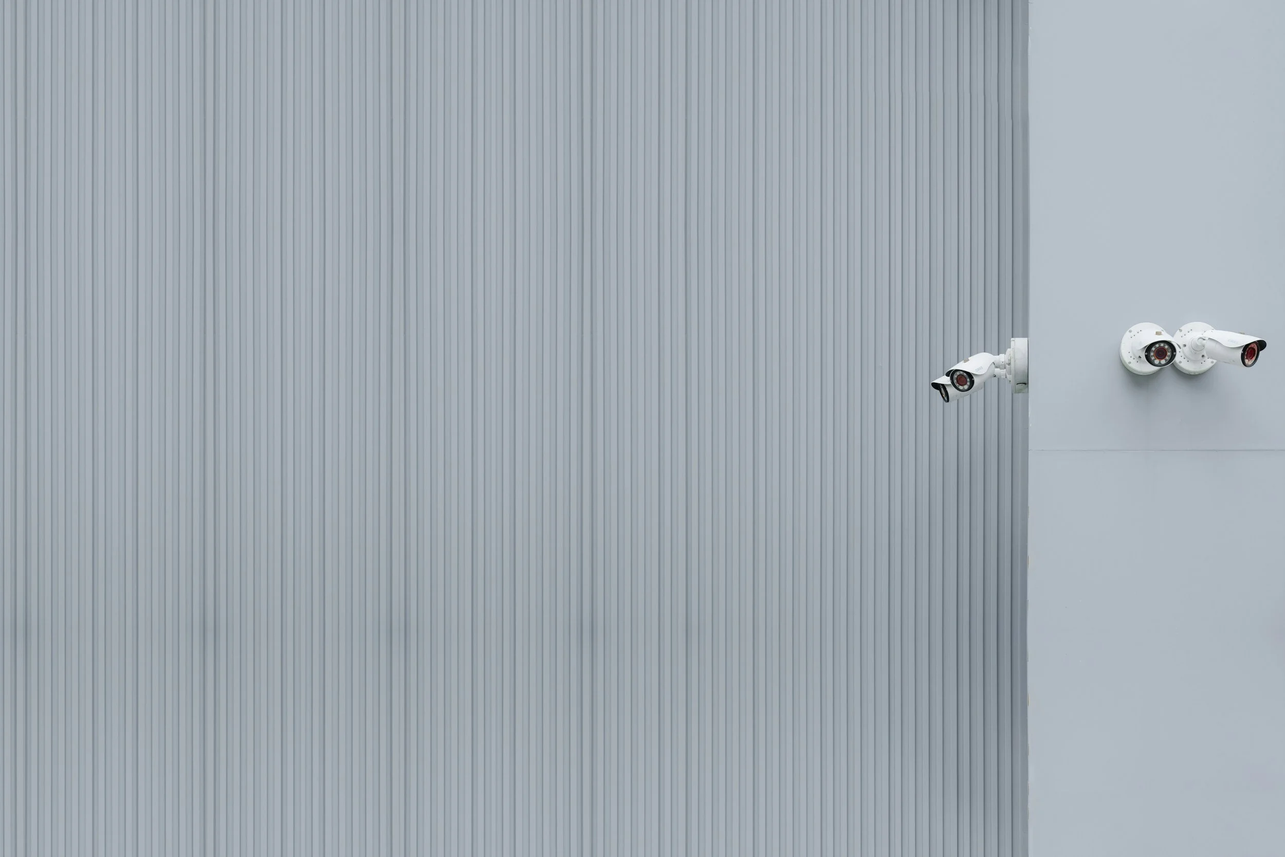 White security cameras mounted on a light gray industrial building exterior