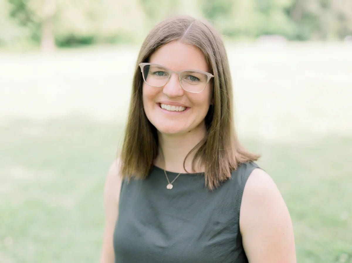 Smiling woman wearing glasses and a dark sleeveless top outdoors