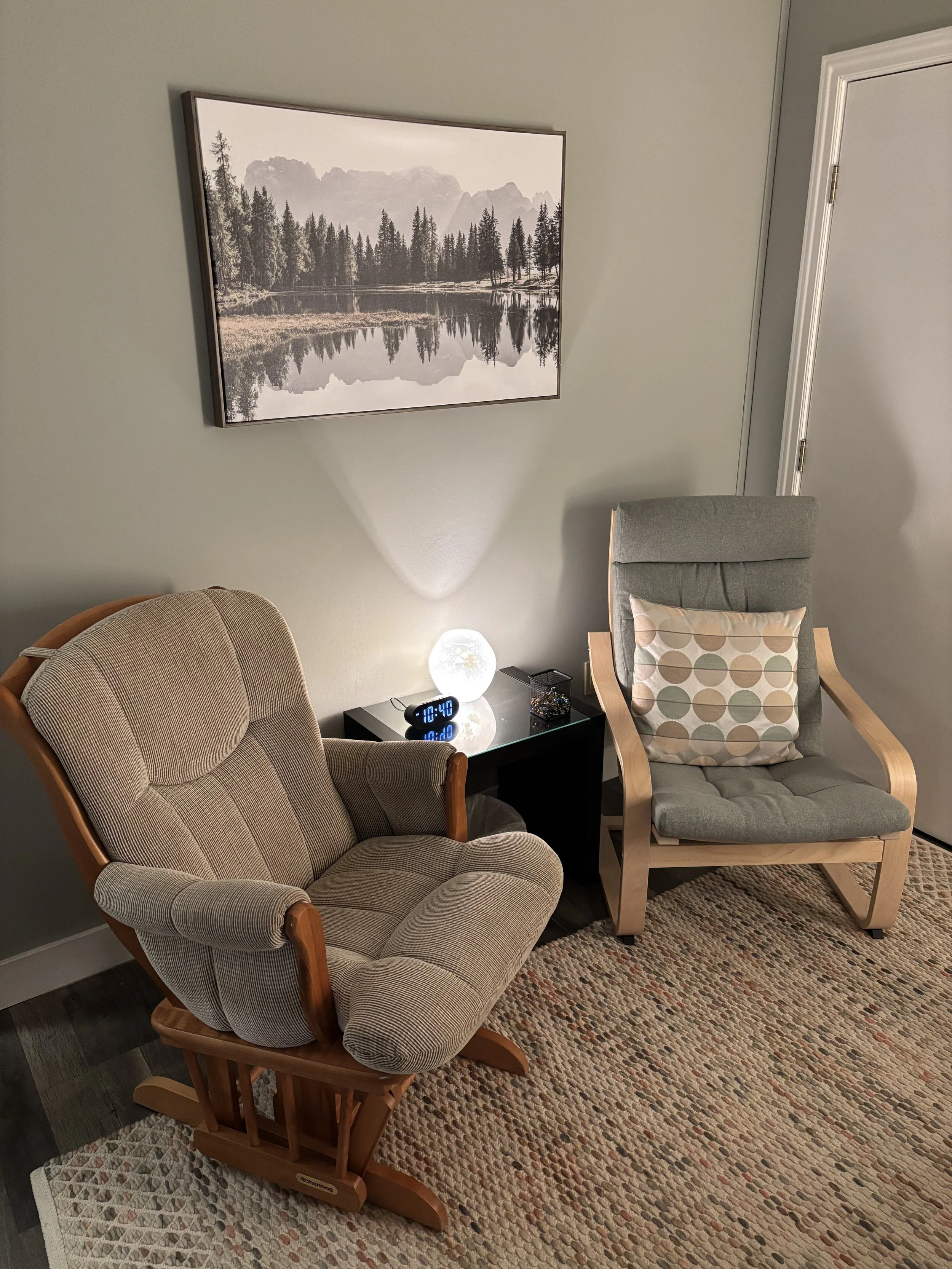 Cozy living room with two upholstered armchairs, a side table and lamp, textured rug, and framed black-and-white mountain landscape photograph.