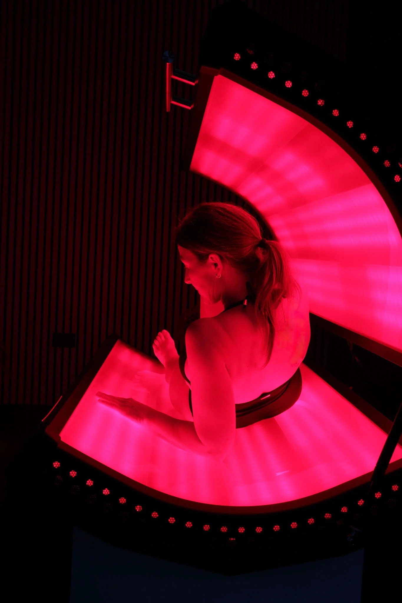 A woman is sitting on a pink-lit circular platform with a domed, glowing pink canopy overhead, creating a futuristic or immersive environment.