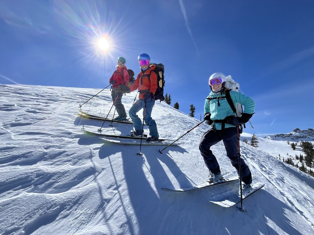 Three people skiing on a snowy mountain under bright sun with clear blue sky.