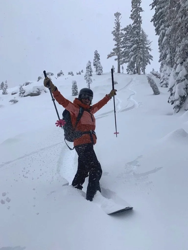 Person snowboarding in a snowy, forested mountain landscape, wearing a helmet, goggles, and winter gear, with arms raised in excitement.
