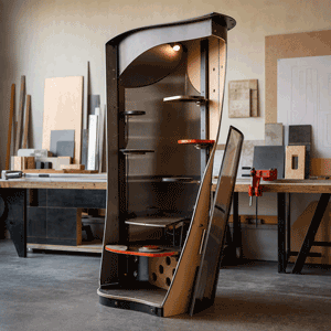 A black, curved, multi-tiered display shelf in a workshop, with various wooden samples and tools nearby.