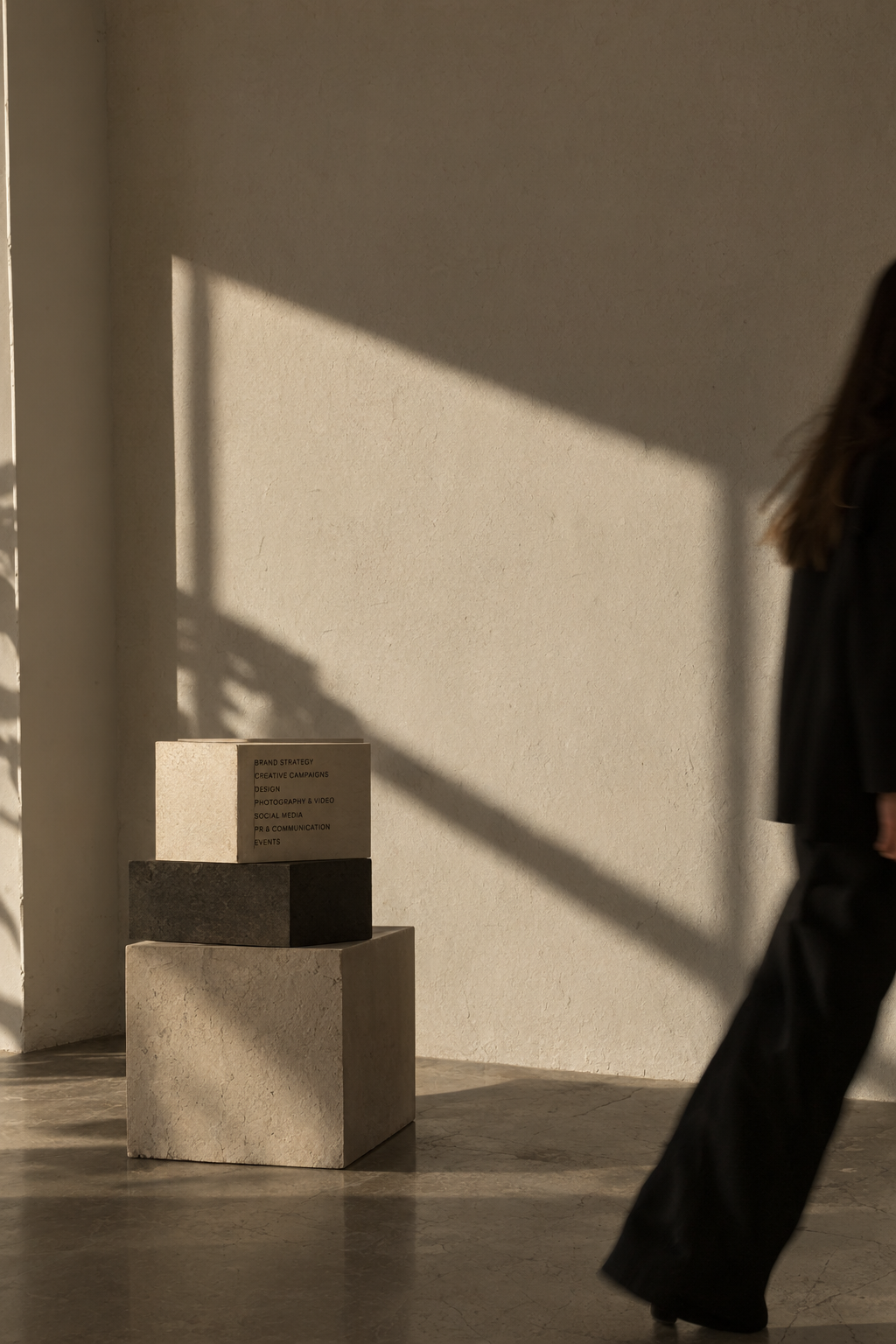 Pessoa a passar por composição arquitetónica minimalista com blocos e sombras, associada à direção criativa e estratégia de marca da Kriyā Projects.
