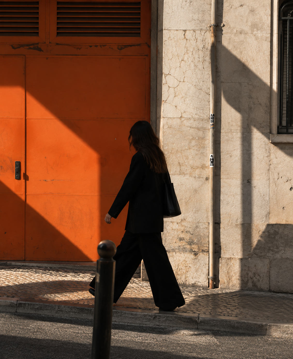 Pessoa a caminhar junto a arquitetura urbana com porta laranja, imagem editorial da identidade visual da Kriyā Projects.