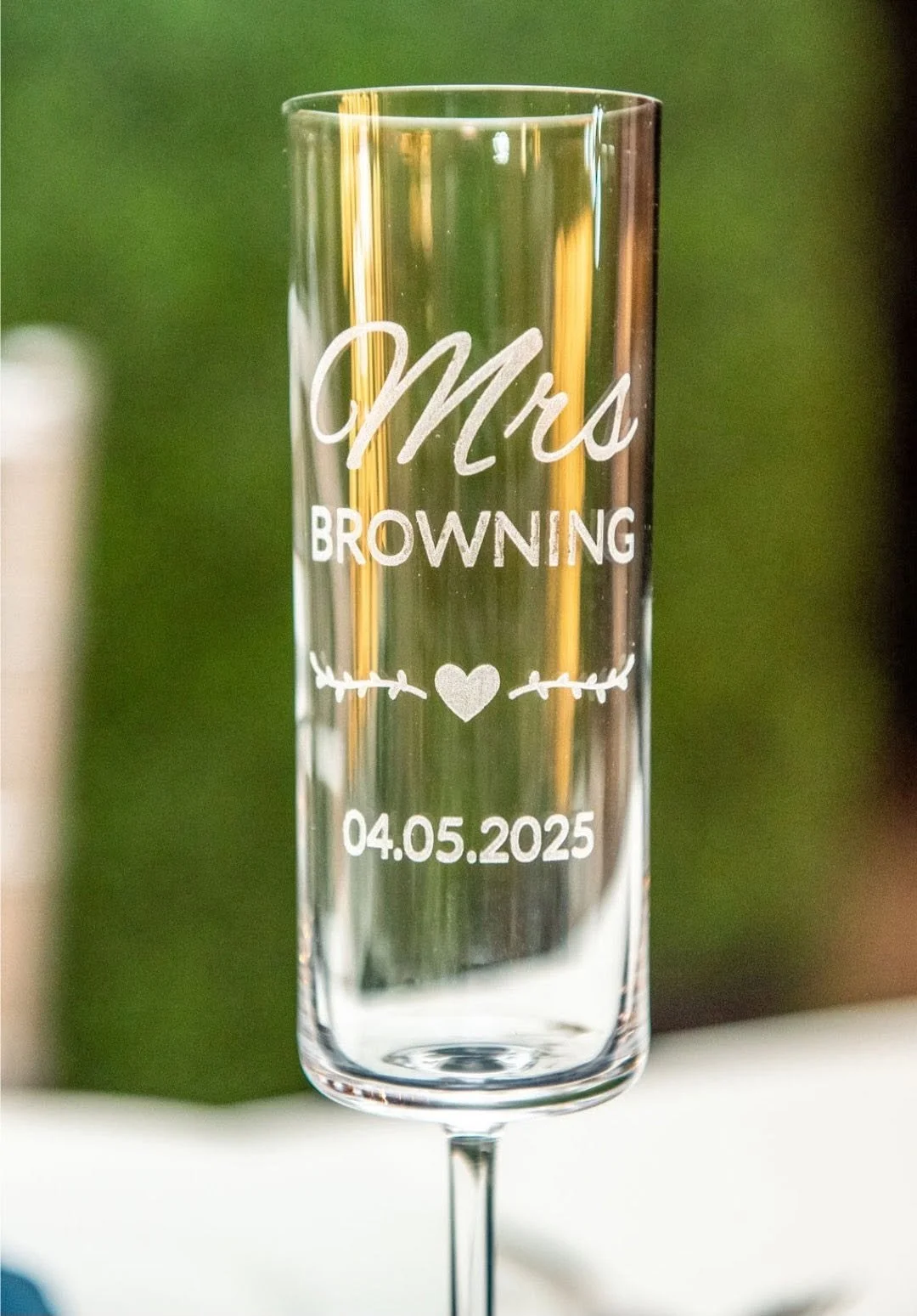 A clear champagne flute engraved with the words 'Mrs. Browning,' a heart, and the date 04.05.2025, likely for a wedding or special celebration.