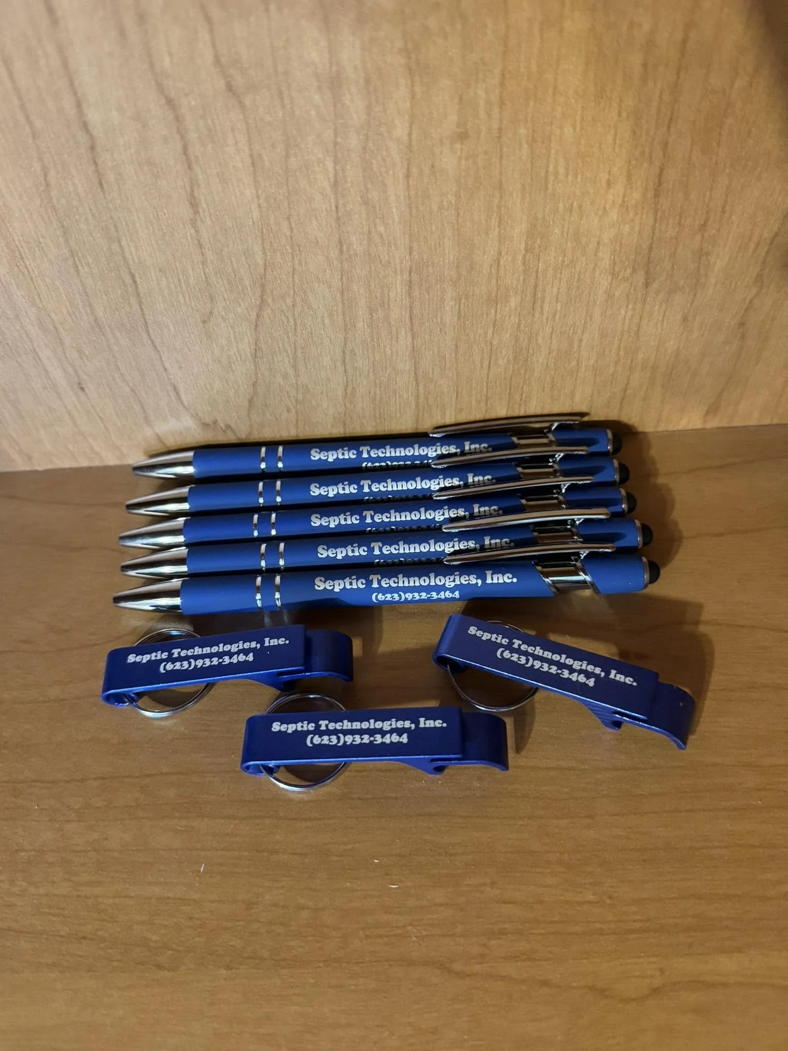 Six blue promotional pens stacked on a wooden surface, each with white text reading 'Septic Technologies, Inc.' and a phone number.
