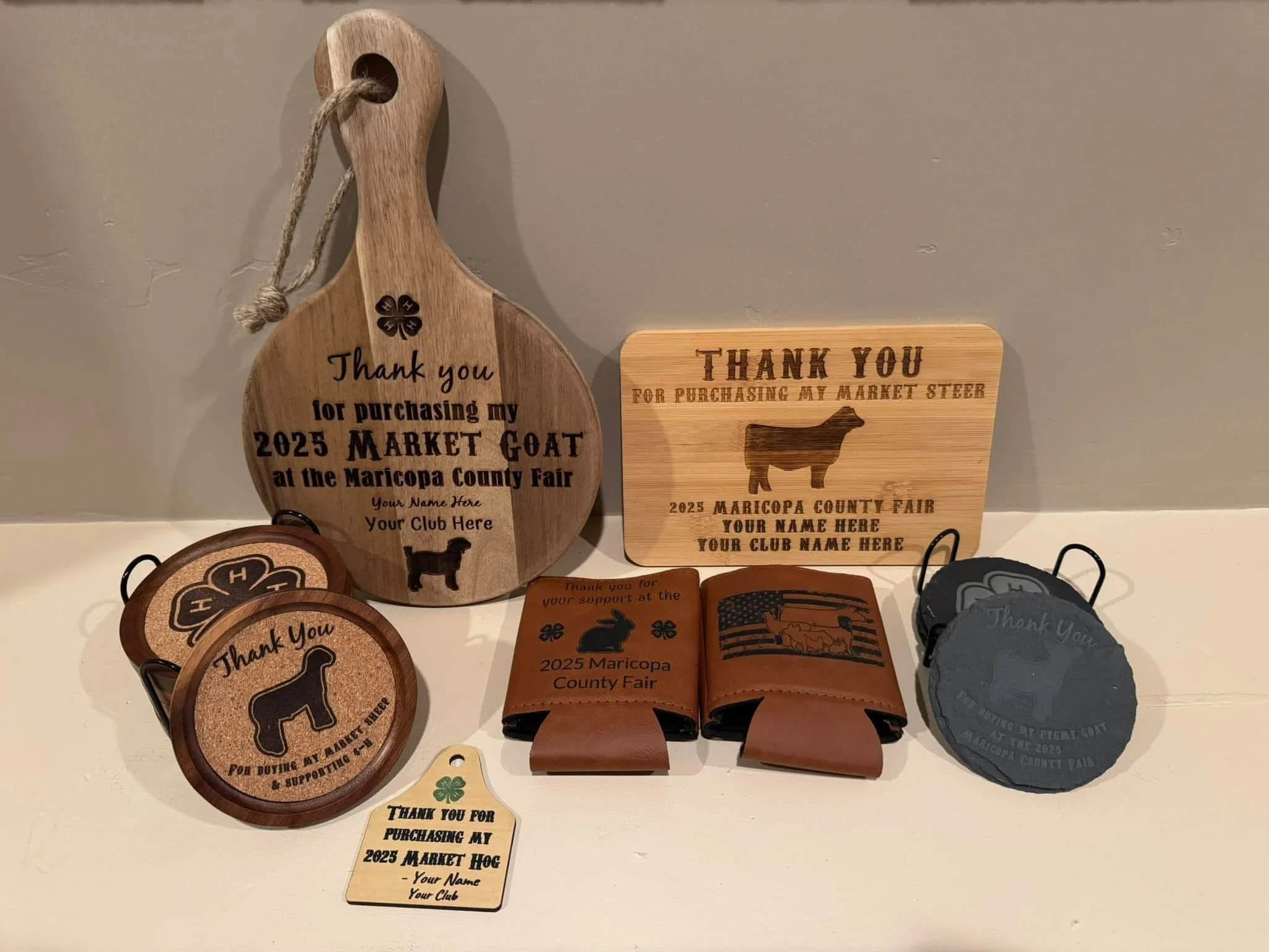 Various wooden and leather items with engraved or printed texts, including thank you signs from the 2025 Maricopa County Fair with themes like market goat, market hog, and other support messages.