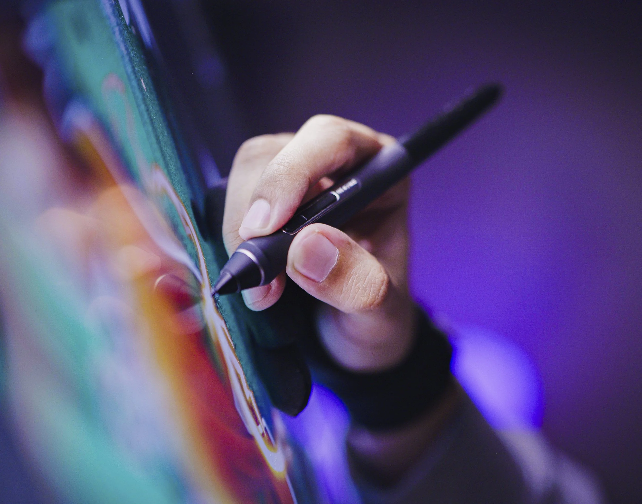 A person holding a stylus pen and drawing on a digital tablet or smartphone with a colorful, abstract background on the device's screen.