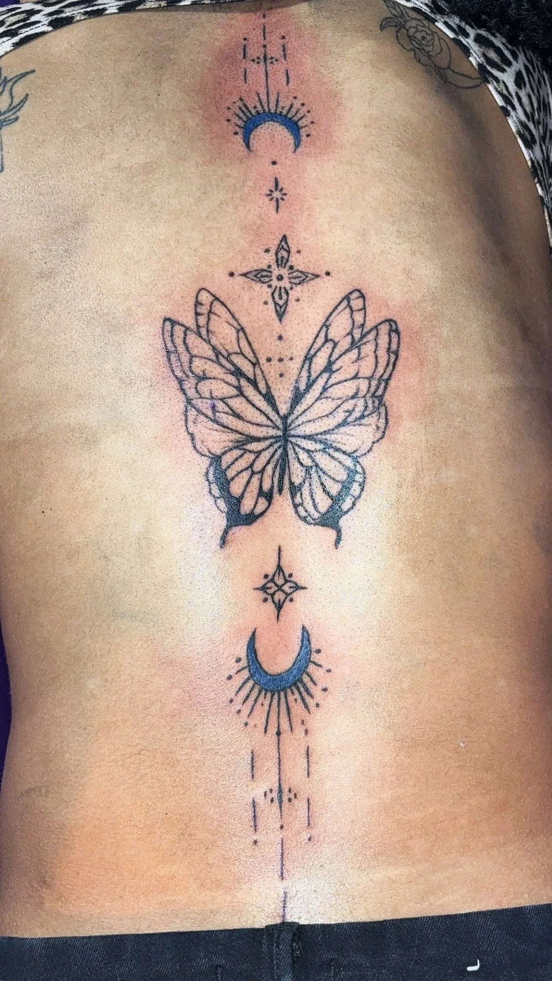 Tattoo of a butterfly with geometric designs and celestial elements on a person's torso.