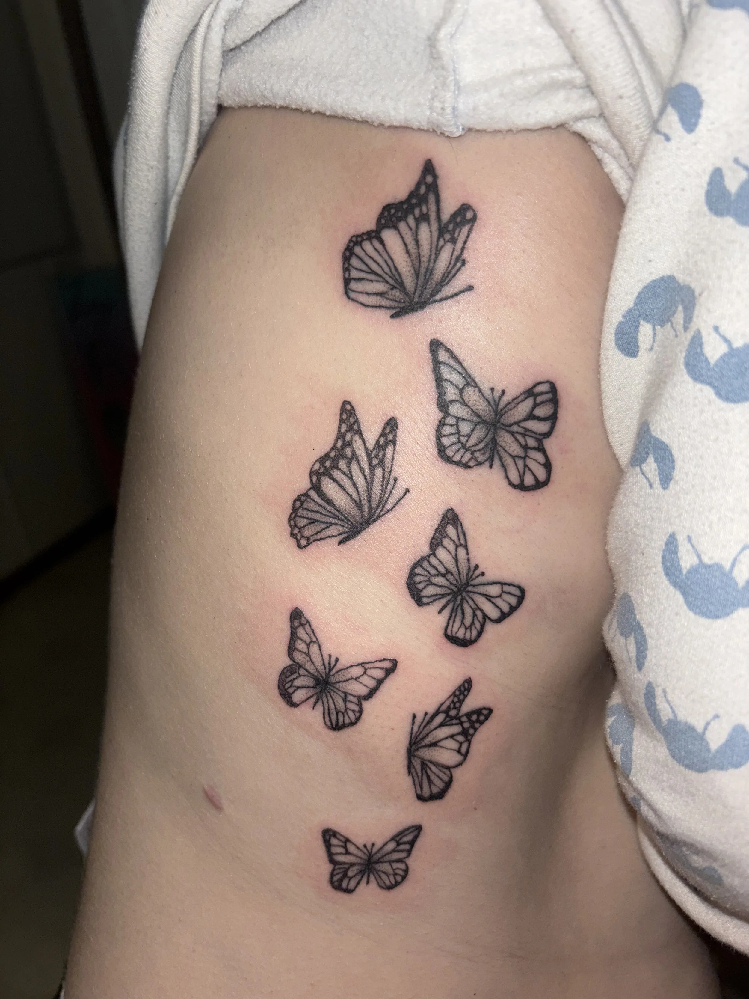 Black ink butterfly tattoo on person's inner arm, with several butterflies arranged vertically.