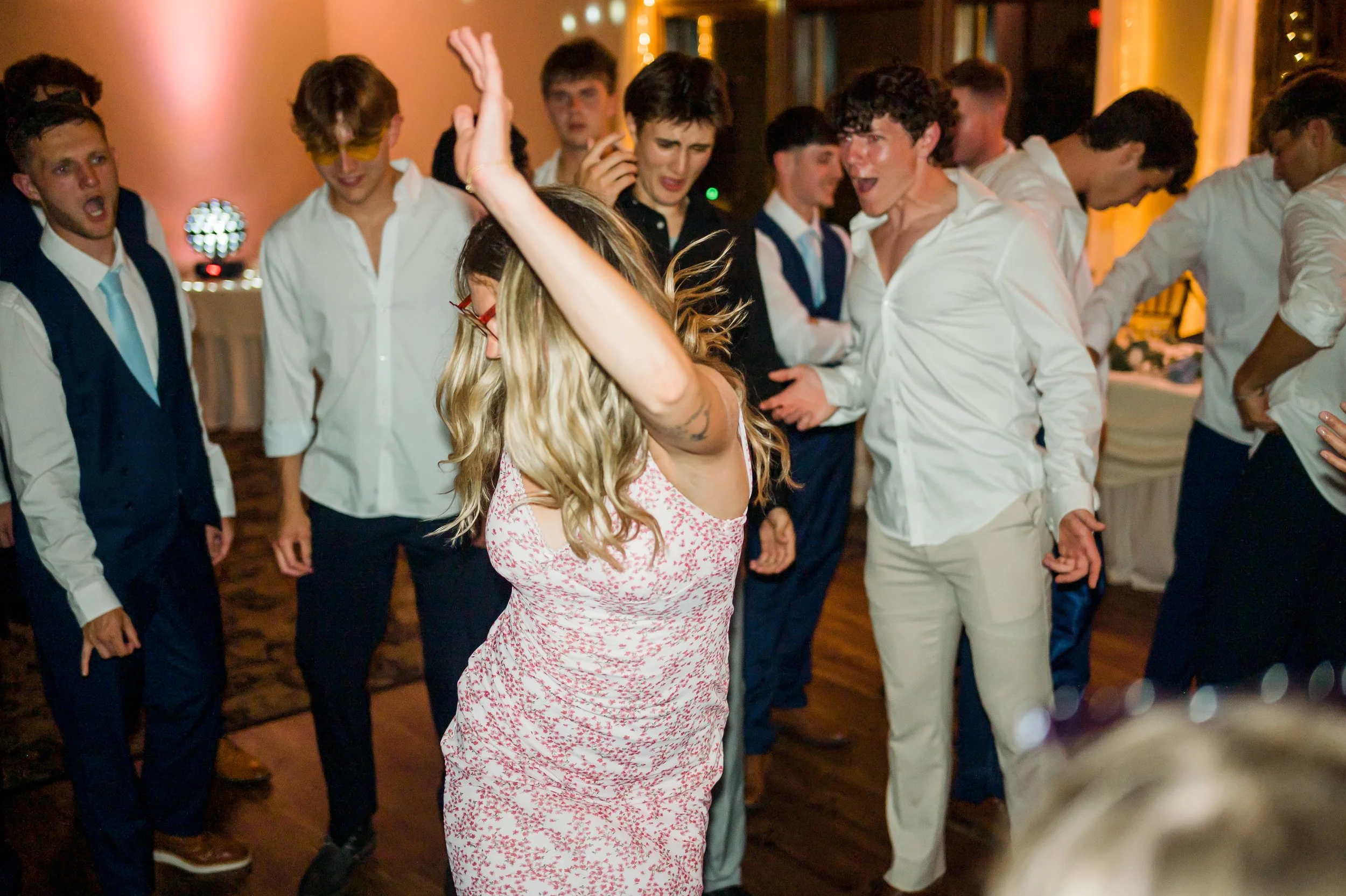 People dancing at a party or celebration, with a woman in the foreground dancing and men in the background singing or enjoying the music.
