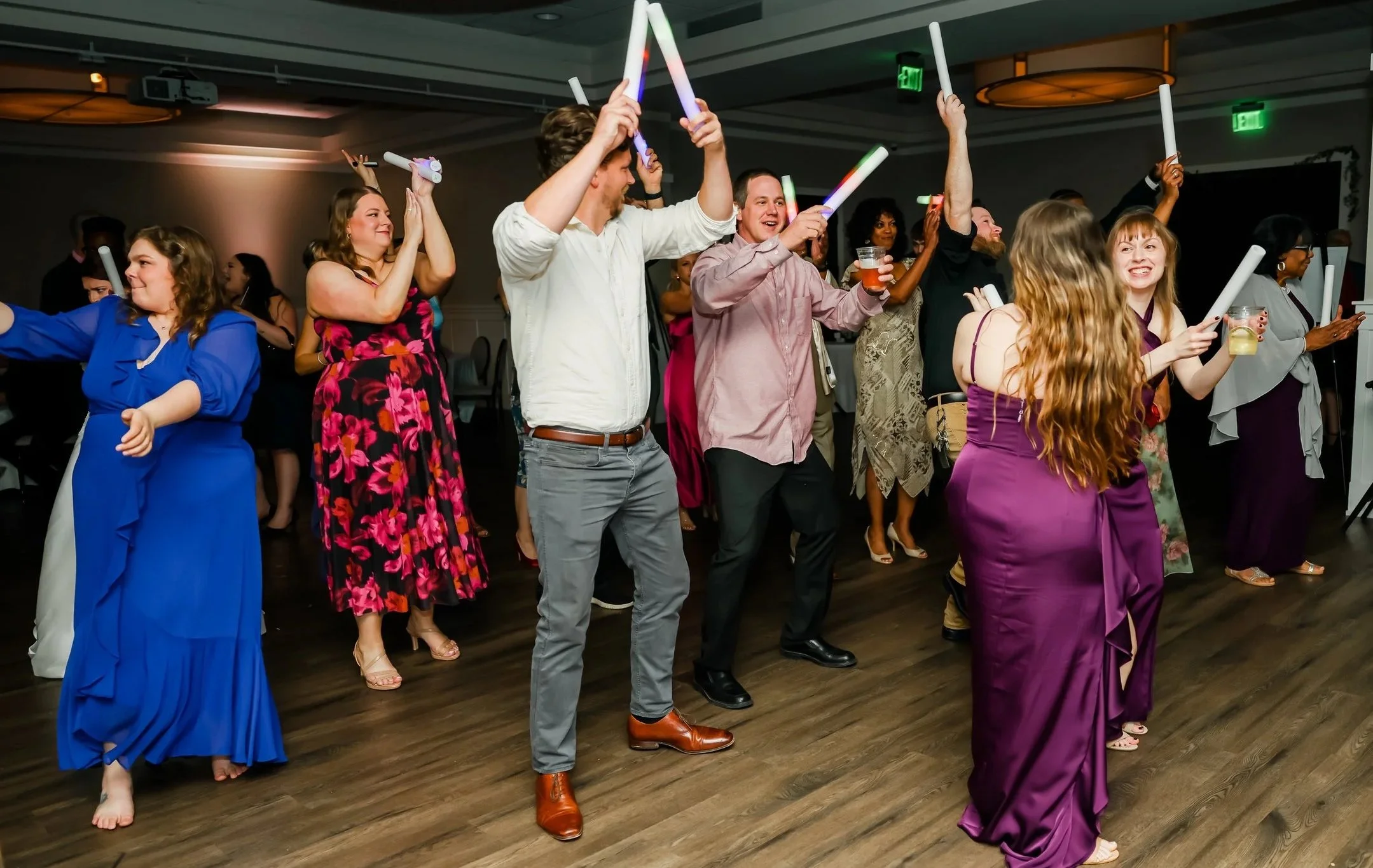 People dancing at a celebration, holding glow sticks and drinks in a decorated indoor venue.