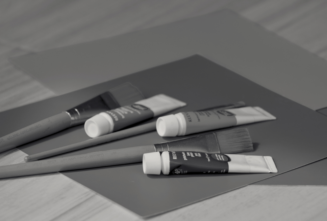 A collection of paint supplies and papers on a table, including paint tubes, paintbrushes, and sheets of paper.