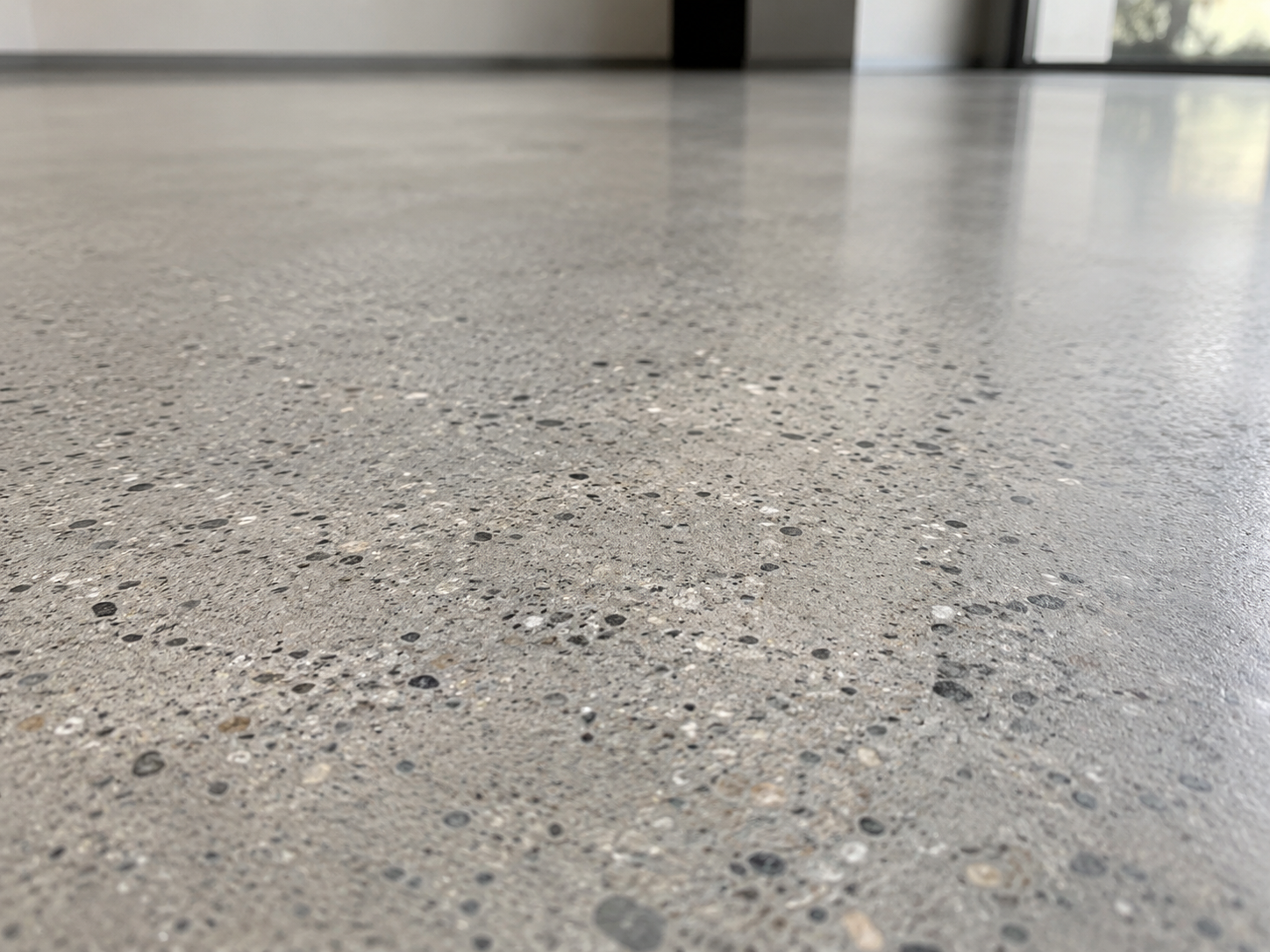 Close-up of a smooth, polished concrete floor in an indoor space with a glass door and natural light in the background.